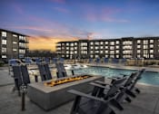 Thumbnail 42 of 43 - A poolside area with chairs and a fire pit in front of a building.