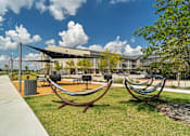 Thumbnail 5 of 53 - A park with a hammock and a building in the background.