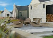 Thumbnail 22 of 63 - A patio with chairs and umbrellas is in front of a house.