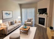 Thumbnail 1 of 10 - A living room with a white couch, a coffee table, and a fireplace.