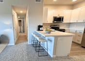Thumbnail 7 of 10 - A kitchen with white cabinets and a white island with a bowl of fruit on it.
