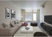Thumbnail 3 of 13 - A living room with a grey couch, a white coffee table, and a flat screen TV.