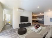 Thumbnail 4 of 13 - A modern living room with a flat screen TV and a brown ottoman.
