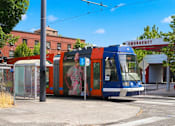 Thumbnail 24 of 35 - A blue and orange tram is parked in front of a building with an emergency sign on it.