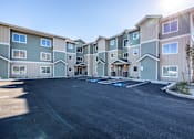 Thumbnail 6 of 6 - A sunny day at a large apartment complex with a parking lot in front.