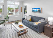 Thumbnail 30 of 35 - A living room with a grey couch, a green chair, a white coffee table, and a painting on the wall.