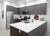 Thumbnail 31 of 35 - A modern kitchen with a white countertop and stainless steel appliances.