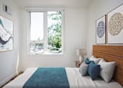 Thumbnail 27 of 30 - The Wes Gresham Oregon Apartments A bedroom with a large bed and a window overlooking a tree-filled street.