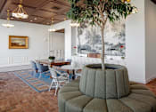 Thumbnail 17 of 35 - A tree in a pot sits on a round ottoman in a room with a painting on the wall.