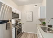 Thumbnail 2 of 7 - A modern kitchen with a stainless steel refrigerator and white cabinets.
