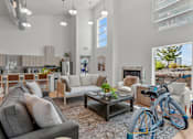 Thumbnail 5 of 38 - A modern living room with a grey sofa, wooden chairs, and a bicycle.