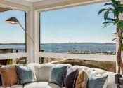 Thumbnail 8 of 26 - Vela Apartments living room with a couch and a large window with a view of a body of water
