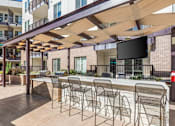 Thumbnail 21 of 23 - A patio with a bar and chairs under a wooden canopy.