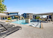 Thumbnail 16 of 20 - A pool area with sun loungers and a building in the background.