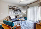 Thumbnail 3 of 20 - A living room with a blue couch, a chair, a table, and a painting on the wall.