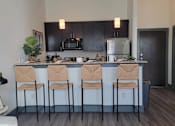 Thumbnail 1 of 27 - A kitchen with black cabinets and a bar area with four chairs at Urban Square, Denton, TexasX, 76210