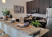 Thumbnail 2 of 27 - A modern kitchen with agranite countertop and stainless steel appliances at Urban Square, Denton, TX, 76210