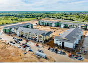 Thumbnail 6 of 11 - A construction site with partially completed buildings and a parking lot with several cars.