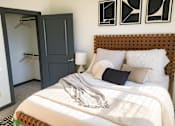 Thumbnail 4 of 19 - A bedroom with a bed, a wardrobe, and a wall-mounted shelf.