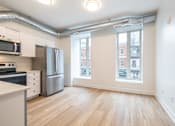 Thumbnail 3 of 20 - an empty living room with a kitchen with stainless steel appliances and a large window