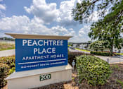 Thumbnail 16 of 25 - A sign for Peachtree Place Apartment Homes in front of a tree.