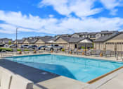 Thumbnail 46 of 46 - A swimming pool surrounded by lounge chairs and umbrellas in front of a row of houses.
