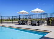 Thumbnail 2 of 46 - A pool with chairs and umbrellas is surrounded by a black fence.