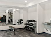 Thumbnail 33 of 98 - A gym room with a bench, weights, and a mirror at The Beaumont Apartments, Bozeman