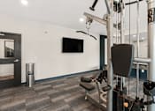 Thumbnail 35 of 98 - A gym with a television and a row of exercise machines at The Beaumont Apartments, Montana