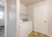 Thumbnail 2 of 23 - A white laundry machine sits in a small room with a door and a window.