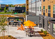 Thumbnail 70 of 98 - A patio with orange chairs and tables is surrounded by buildings at The Beaumont Apartments, Bozeman, 59715