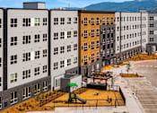 Thumbnail 61 of 98 - A playground area with a slide and a swing set is located in the courtyard of apartment buildings at The Beaumont Apartments, Bozeman, Montana 59715