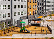 Thumbnail 58 of 98 - A playground with a grey slide and play area with woodchip flooring at The Beaumont Apartments, Bozeman, Montana 59715