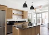 Thumbnail 1 of 26 - a kitchen with wooden cabinets and a large island with a black countertop at The Alloy at Geneva, Vineyard, 84058