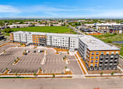 Thumbnail 88 of 98 - A large multi-story building with a parking lot in front at The Beaumont Apartments, Montana