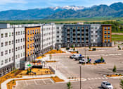 Thumbnail 56 of 98 - A parking lot in front of apartment buildings with a playground and mountains in the background at The Beaumont Apartments, MT 59715
