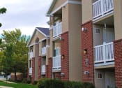 Thumbnail 5 of 5 - View of Country Oaks apartment building 4 with red brick, white beam balconies, and manicured grass pathways with trees at Country Oaks Apartments in Clearfield, Utah 84015