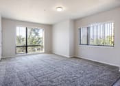 Thumbnail 3 of 23 - A spacious room with a large carpeted floor and two windows.