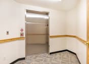 Thumbnail 29 of 31 - a stainless steel elevator in a white walled room with a wooden railing