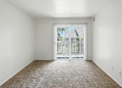 Thumbnail 15 of 26 - A room with a carpeted floor and a sliding glass door leading to a balcony.at Country Oaks Apartments, Clearfield, UT