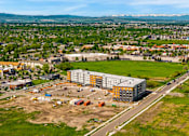 Thumbnail 80 of 98 - A large building with a grey and yellow exterior is surrounded by a parking lot and construction equipment at The Beaumont Apartments, Montana