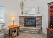 Thumbnail 22 of 28 - A cozy living room with a stone fireplace and a side table with a lamp.