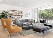 Thumbnail 6 of 29 - A living room with a grey couch, a wooden chair, a black bench, and a glass table.
