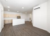 Thumbnail 24 of 29 - A spacious room with wooden flooring and a kitchen area with white cabinets.