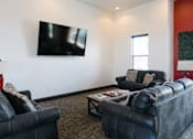 Thumbnail 10 of 28 - A black leather couch sits in a living room with a flat screen TV mounted on the wall.