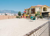 Thumbnail 7 of 28 - A playground with a slide and swings in front of a building with a mountain in the background.