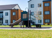 Thumbnail 59 of 64 - A playground with a slide and a bench in front of a building. at Silverbrook Apartments, Kalispell, MT, 59901