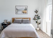 Thumbnail 10 of 64 - A bed with a grey comforter and two pillows sits in a room with a framed picture of a snowy landscape on the wall. at Silverbrook Apartments, Kalispell 59901