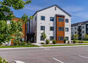 Thumbnail 63 of 64 - A modern building with a white facade and a brown door is surrounded by other buildings and trees. at Silverbrook Apartments, Kalispell, MT, 59901