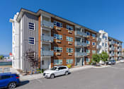 Thumbnail 2 of 31 - A modern apartment building with cars parked in front.